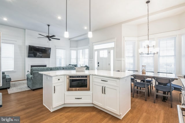 kitchen featuring a kitchen island, white cabinets, light hardwood / wood-style floors, oven, and hanging light fixtures