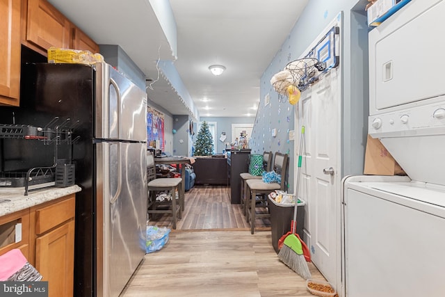 kitchen with stainless steel refrigerator, stacked washing maching and dryer, light hardwood / wood-style floors, and light stone counters