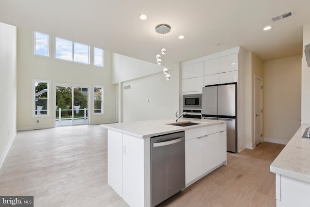 kitchen with light hardwood / wood-style flooring, an island with sink, decorative light fixtures, white cabinetry, and stainless steel appliances