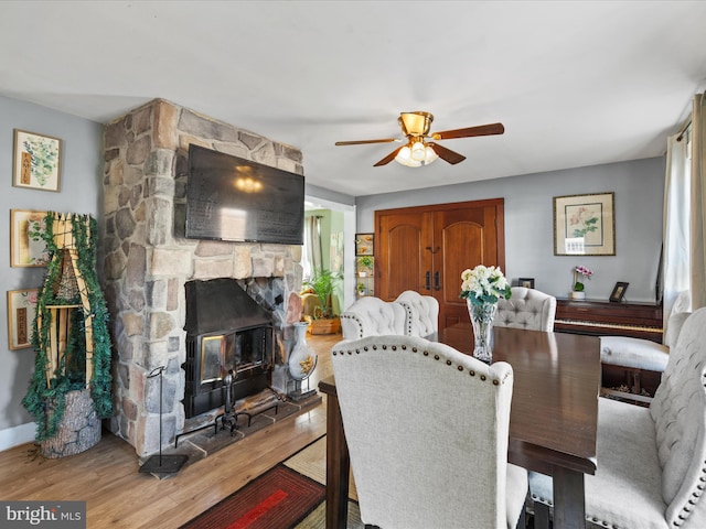 dining space with hardwood / wood-style flooring, ceiling fan, and a stone fireplace