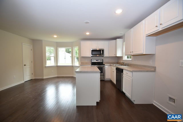 kitchen featuring dark wood-type flooring, sink, appliances with stainless steel finishes, a kitchen island, and white cabinetry