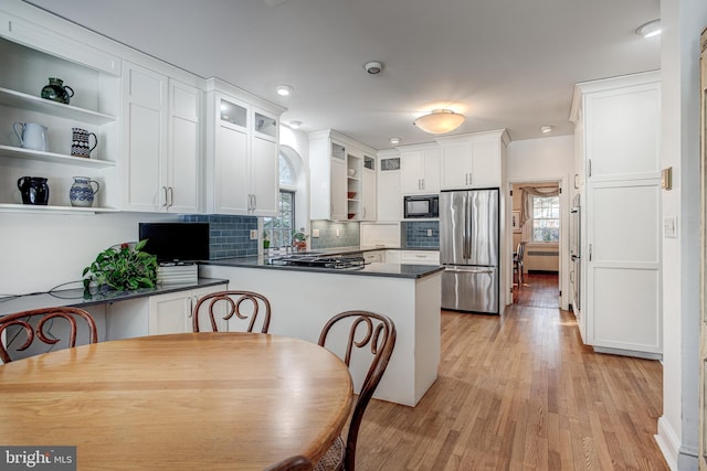 kitchen featuring light hardwood / wood-style flooring, stainless steel refrigerator, white cabinetry, black microwave, and kitchen peninsula