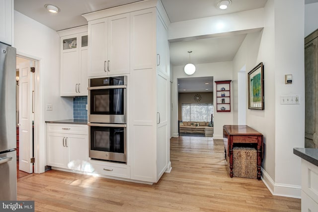 kitchen featuring white cabinets, decorative backsplash, hanging light fixtures, light hardwood / wood-style floors, and stainless steel appliances