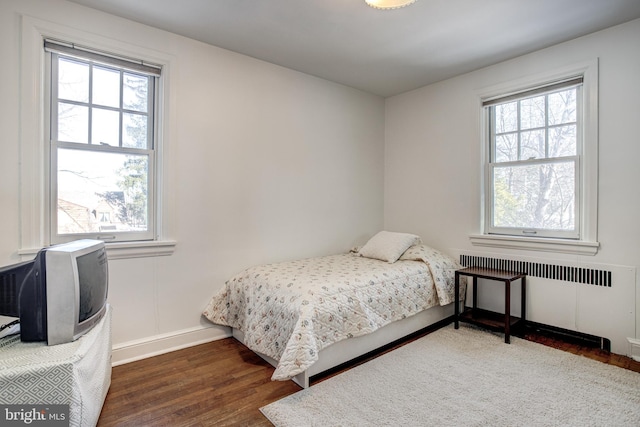 bedroom with multiple windows, radiator, and dark hardwood / wood-style floors