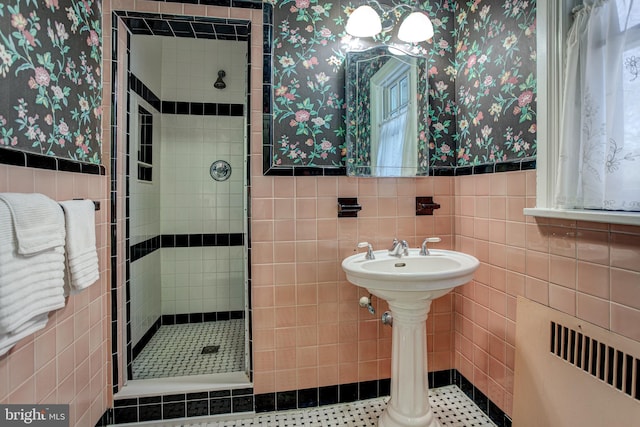 bathroom featuring radiator heating unit, a shower with shower door, sink, and tile walls