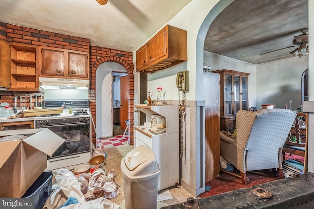 kitchen featuring white gas range, ceiling fan, and brick wall