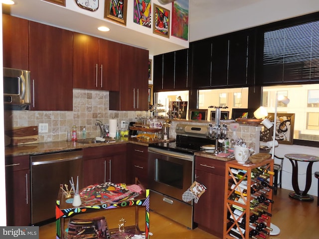 kitchen with decorative backsplash, appliances with stainless steel finishes, light wood-type flooring, sink, and stone countertops