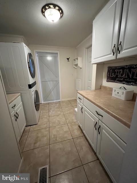 laundry area featuring light tile patterned flooring, cabinets, and stacked washer / dryer