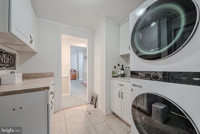 laundry area featuring cabinets, light tile patterned floors, stacked washer and dryer, and ornamental molding