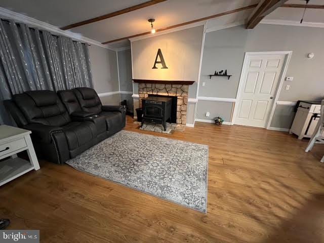 living room featuring a wood stove, ornamental molding, lofted ceiling with beams, and hardwood / wood-style flooring