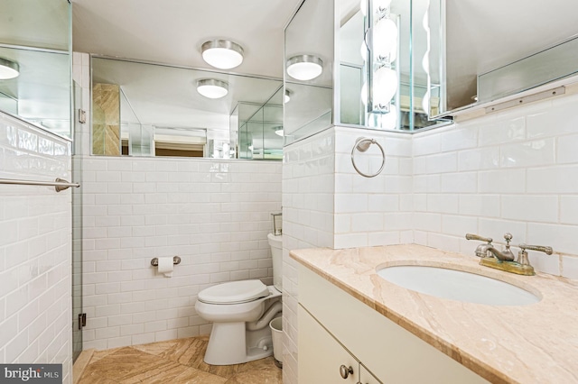 bathroom with vanity, a shower with shower door, tile walls, and toilet