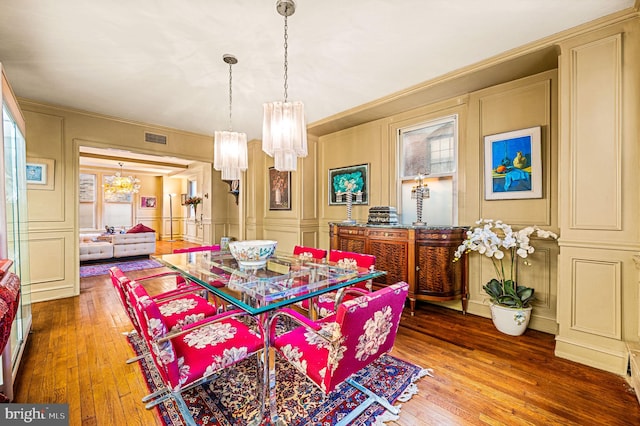 dining space with a decorative wall, visible vents, wood-type flooring, and ornamental molding