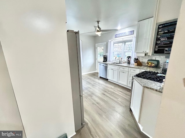 kitchen featuring white cabinets, light hardwood / wood-style flooring, appliances with stainless steel finishes, tasteful backsplash, and light stone counters