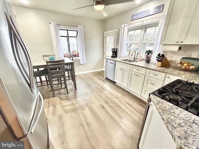 kitchen with sink, appliances with stainless steel finishes, light hardwood / wood-style floors, light stone counters, and white cabinetry