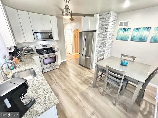 kitchen with white cabinetry, sink, light stone counters, light hardwood / wood-style flooring, and appliances with stainless steel finishes