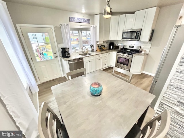 kitchen with decorative light fixtures, stainless steel appliances, white cabinetry, and light hardwood / wood-style flooring