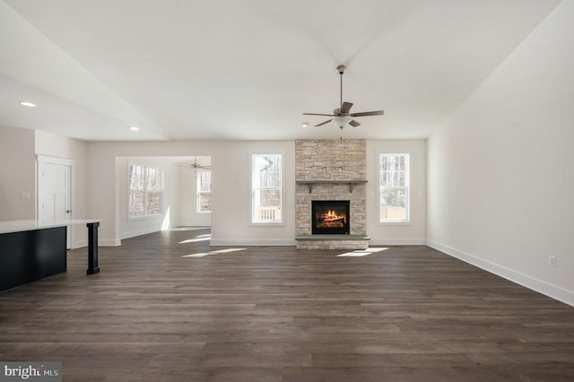 unfurnished living room with ceiling fan, dark hardwood / wood-style floors, and a stone fireplace