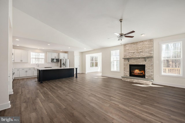 unfurnished living room with ceiling fan, dark hardwood / wood-style flooring, sink, and a stone fireplace