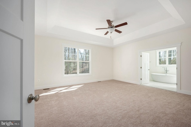 unfurnished bedroom with ceiling fan, a tray ceiling, ensuite bathroom, and light carpet