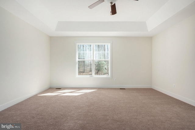 carpeted empty room with a raised ceiling and ceiling fan