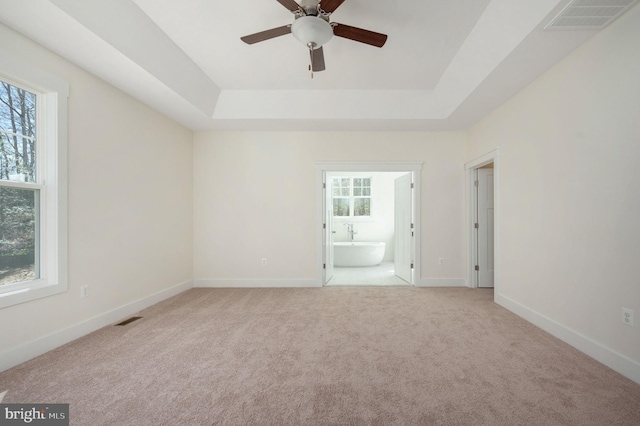 spare room with a raised ceiling, light carpet, and ceiling fan