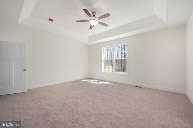 carpeted spare room with ceiling fan and a tray ceiling