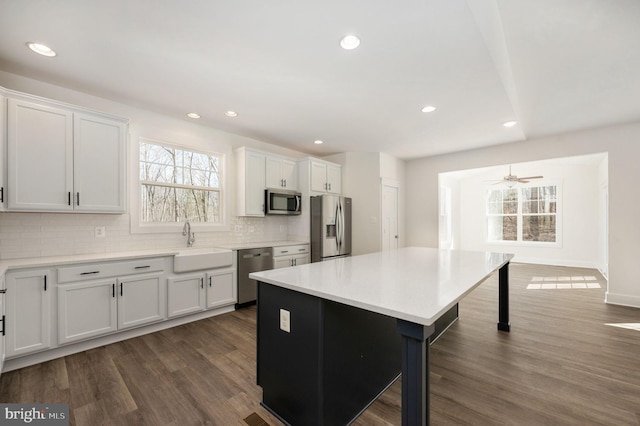 kitchen with white cabinets, appliances with stainless steel finishes, a kitchen island, dark wood-type flooring, and sink