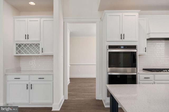 kitchen with black gas stovetop, decorative backsplash, white cabinetry, stainless steel double oven, and light stone counters