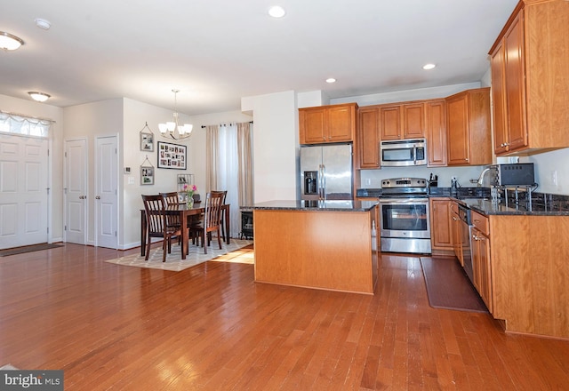 kitchen with stainless steel appliances, wood-type flooring, decorative light fixtures, a notable chandelier, and a center island