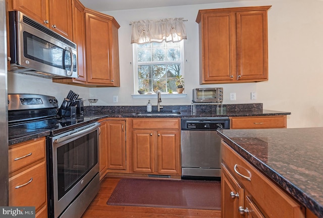 kitchen featuring dark stone countertops, sink, dark wood-type flooring, and appliances with stainless steel finishes