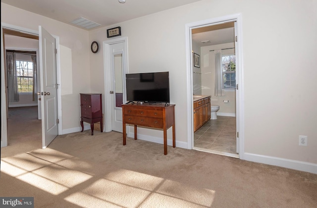 bedroom featuring light carpet, ensuite bath, and multiple windows