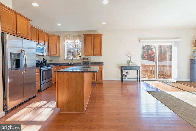 kitchen featuring sink, a center island, stainless steel appliances, dark stone countertops, and light hardwood / wood-style floors