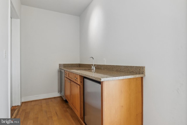 bar with light stone countertops, light hardwood / wood-style floors, stainless steel refrigerator, and sink