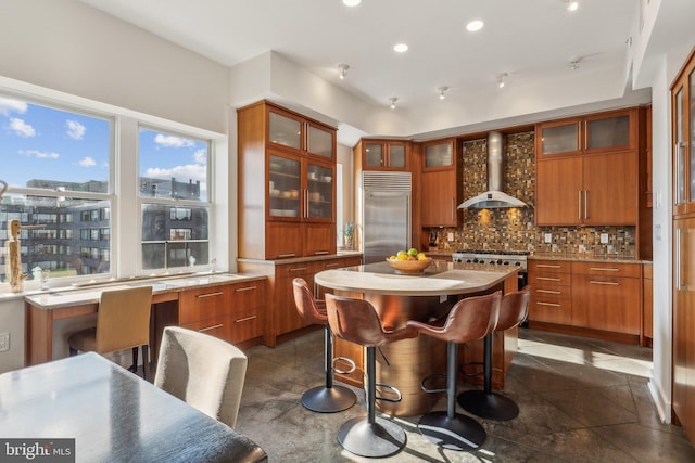 kitchen with backsplash, a kitchen breakfast bar, wall chimney range hood, appliances with stainless steel finishes, and a kitchen island