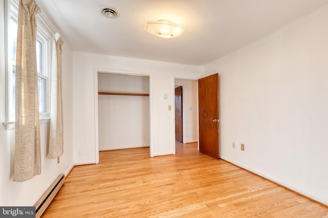 unfurnished bedroom with a closet, light hardwood / wood-style floors, and a baseboard heating unit