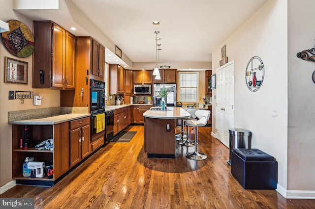 kitchen with pendant lighting, a center island, black appliances, dark hardwood / wood-style floors, and a kitchen bar