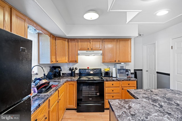 kitchen featuring black appliances, light wood-type flooring, sink, and dark stone counters