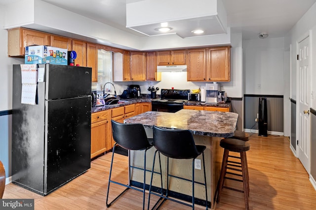 kitchen featuring a kitchen breakfast bar, light wood-type flooring, sink, black appliances, and a center island