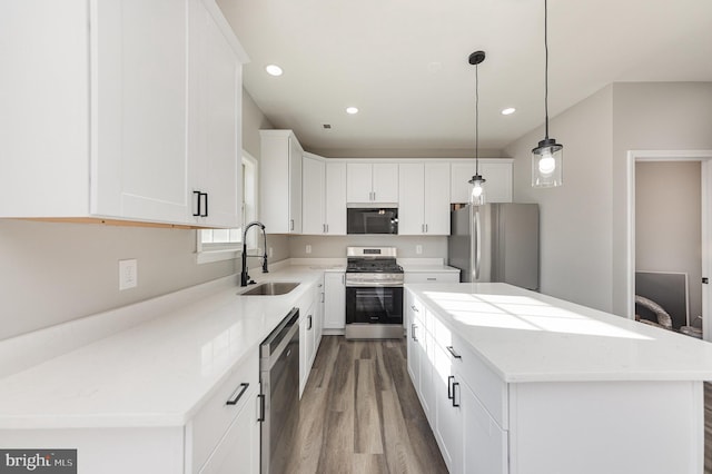 kitchen with stainless steel appliances, sink, white cabinets, a kitchen island, and hanging light fixtures