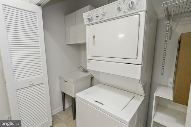 clothes washing area with light tile patterned floors, stacked washer / drying machine, and sink