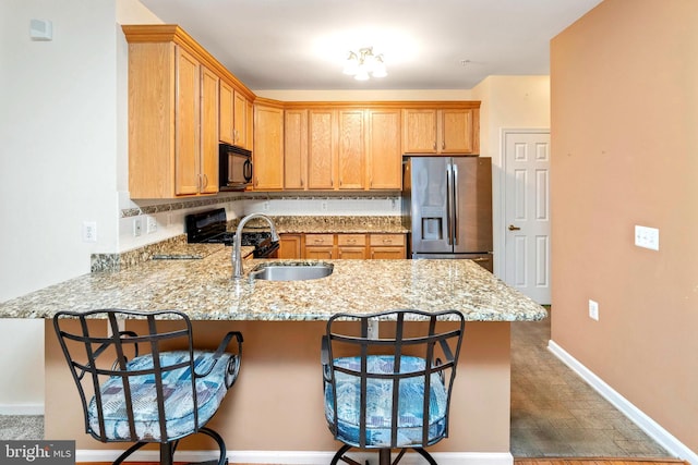 kitchen featuring black appliances, a kitchen breakfast bar, sink, light stone counters, and kitchen peninsula