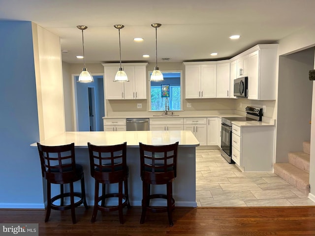 kitchen with a breakfast bar, sink, light wood-type flooring, appliances with stainless steel finishes, and white cabinetry