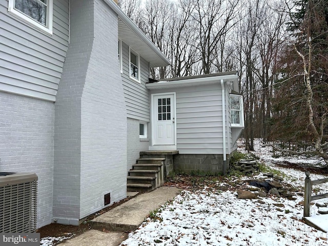 snow covered property entrance with central AC unit