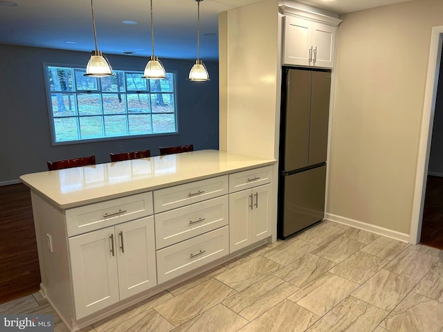 kitchen featuring stainless steel fridge, white cabinets, and hanging light fixtures