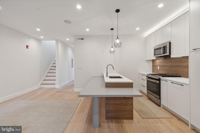 kitchen featuring white cabinets, hanging light fixtures, sink, light wood-type flooring, and appliances with stainless steel finishes