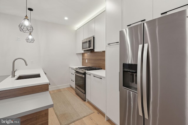 kitchen featuring sink, light wood-type flooring, decorative light fixtures, white cabinetry, and stainless steel appliances