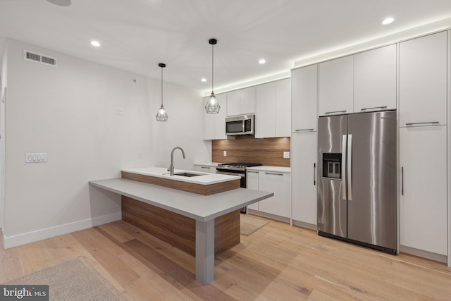 kitchen with sink, light hardwood / wood-style floors, pendant lighting, white cabinets, and appliances with stainless steel finishes