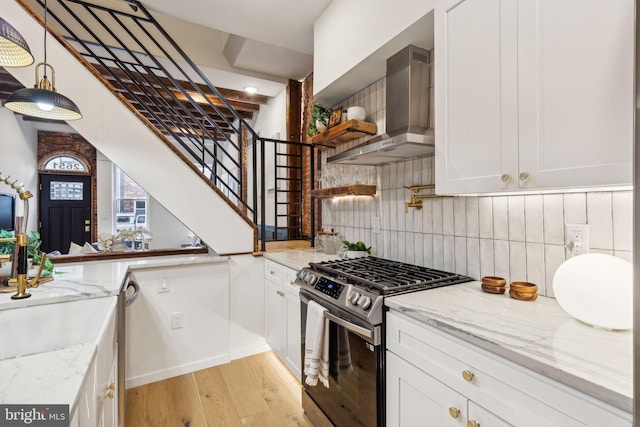 kitchen with light wood-type flooring, light stone counters, stainless steel appliances, wall chimney range hood, and white cabinets