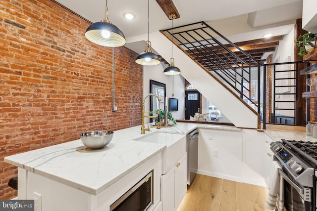 kitchen featuring light stone countertops, brick wall, pendant lighting, light hardwood / wood-style flooring, and white cabinets