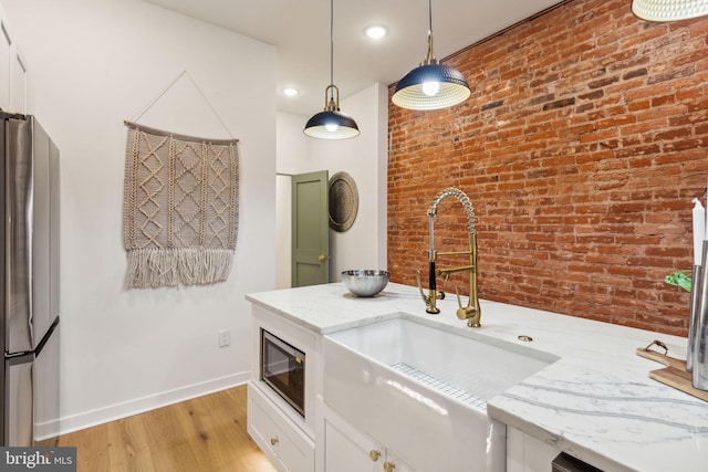 kitchen featuring brick wall, sink, pendant lighting, light hardwood / wood-style floors, and stainless steel refrigerator